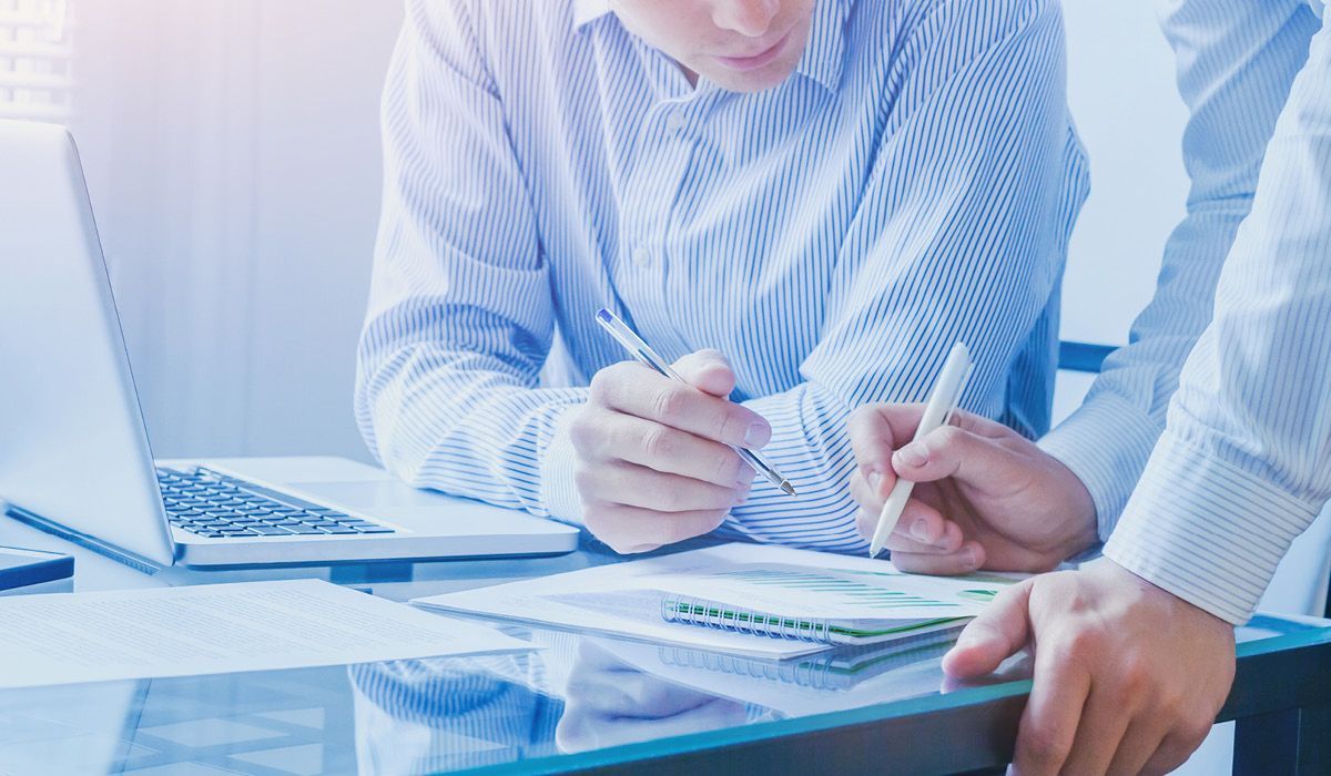 Two people reviewing documents at a glass table beside a laptop, in a bright office.