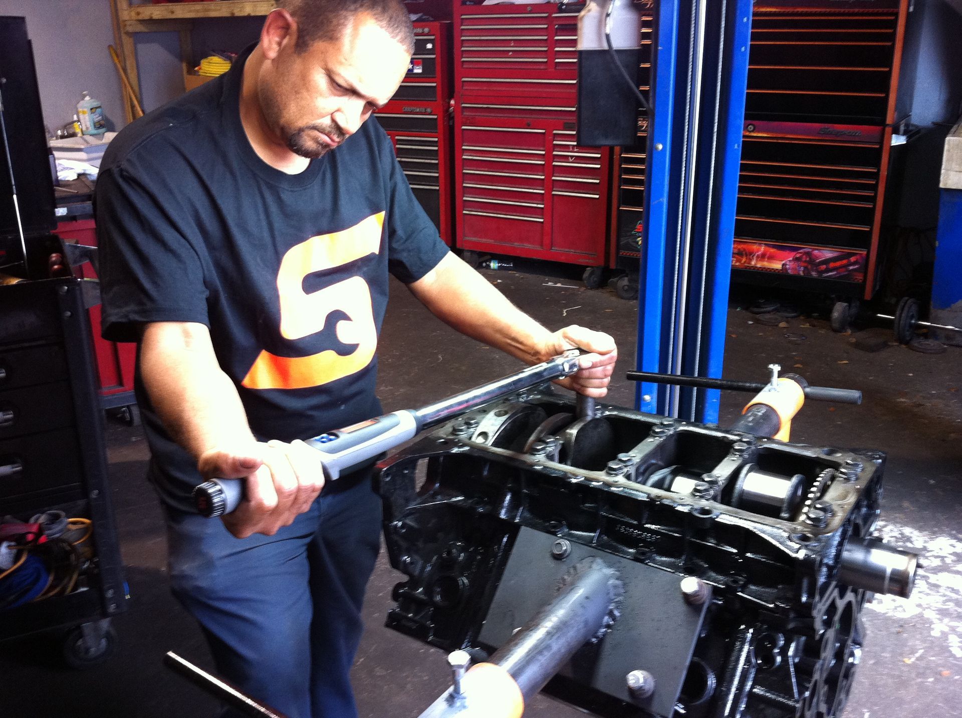 A man wearing a black shirt with the number 5 on it is working on a car engine