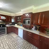 A kitchen with dark wood cabinetry, a built-in microwave, white appliances, and beige rectangular floor tiles.