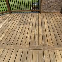 A view of a wooden deck featuring a horizontal border board and vertical planking against a brick wall and railing.