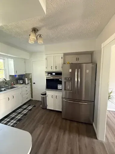 A kitchen with white cabinets, stainless steel appliances, a checkered runner rug, and wood-look flooring.