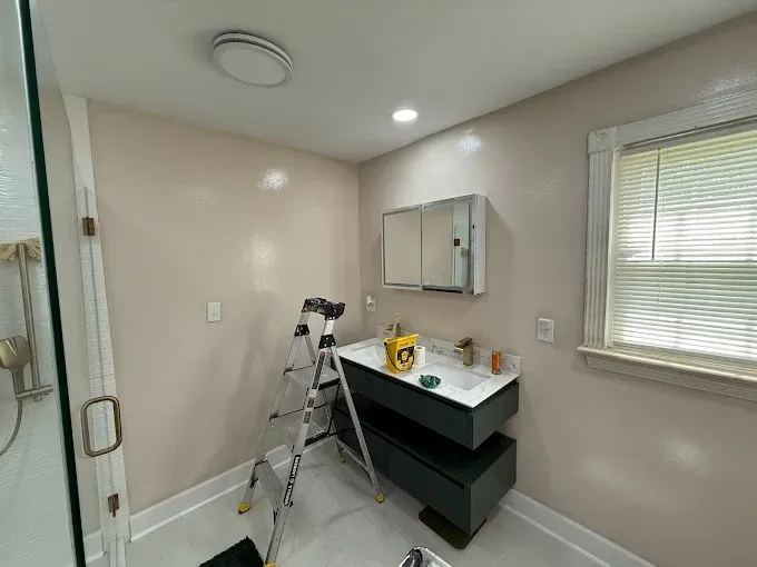 A bathroom with light pink walls, a dark grey floating vanity, a wall-mounted medicine cabinet, and a step ladder.