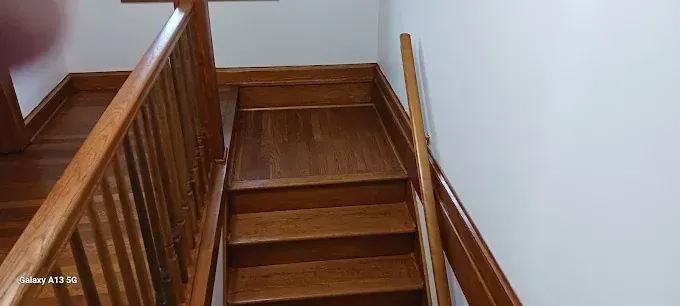 A staircase with wooden steps and railing leading to a small landing next to a white wall.