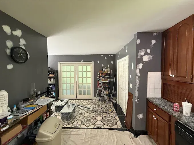 A room with dark gray walls undergoing repairs, featuring visible spackling patches, a patterned rug, and wooden cabinets.