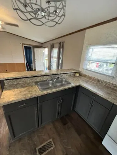 A kitchen featuring charcoal-gray cabinets, light-flecked laminate countertops, a double basin sink, and a modern chandelier.