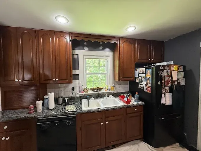A kitchen with dark wood cabinets, blue-grey granite countertops, a white double sink, and a black refrigerator.