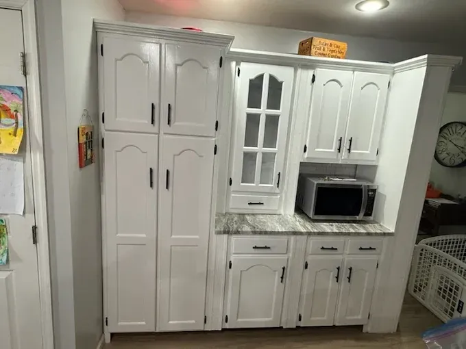 White kitchen cabinetry featuring a tall pantry unit, a glass-front display cabinet, and a built-in microwave nook.
