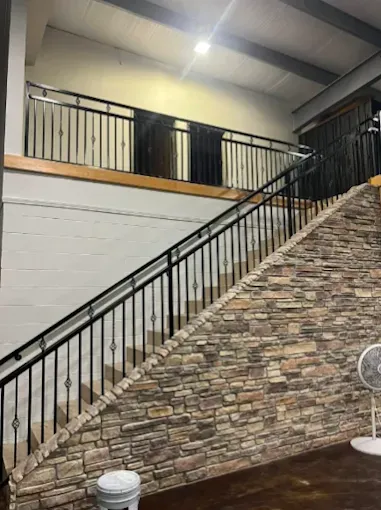 A staircase with a black metal railing and a stone-tiled wall, leading up to a landing in an indoor space.