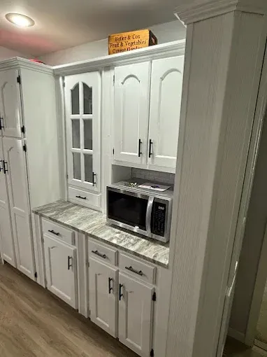 White kitchen cabinets with black handles, a marble-patterned countertop, and a built-in microwave in a residential space.