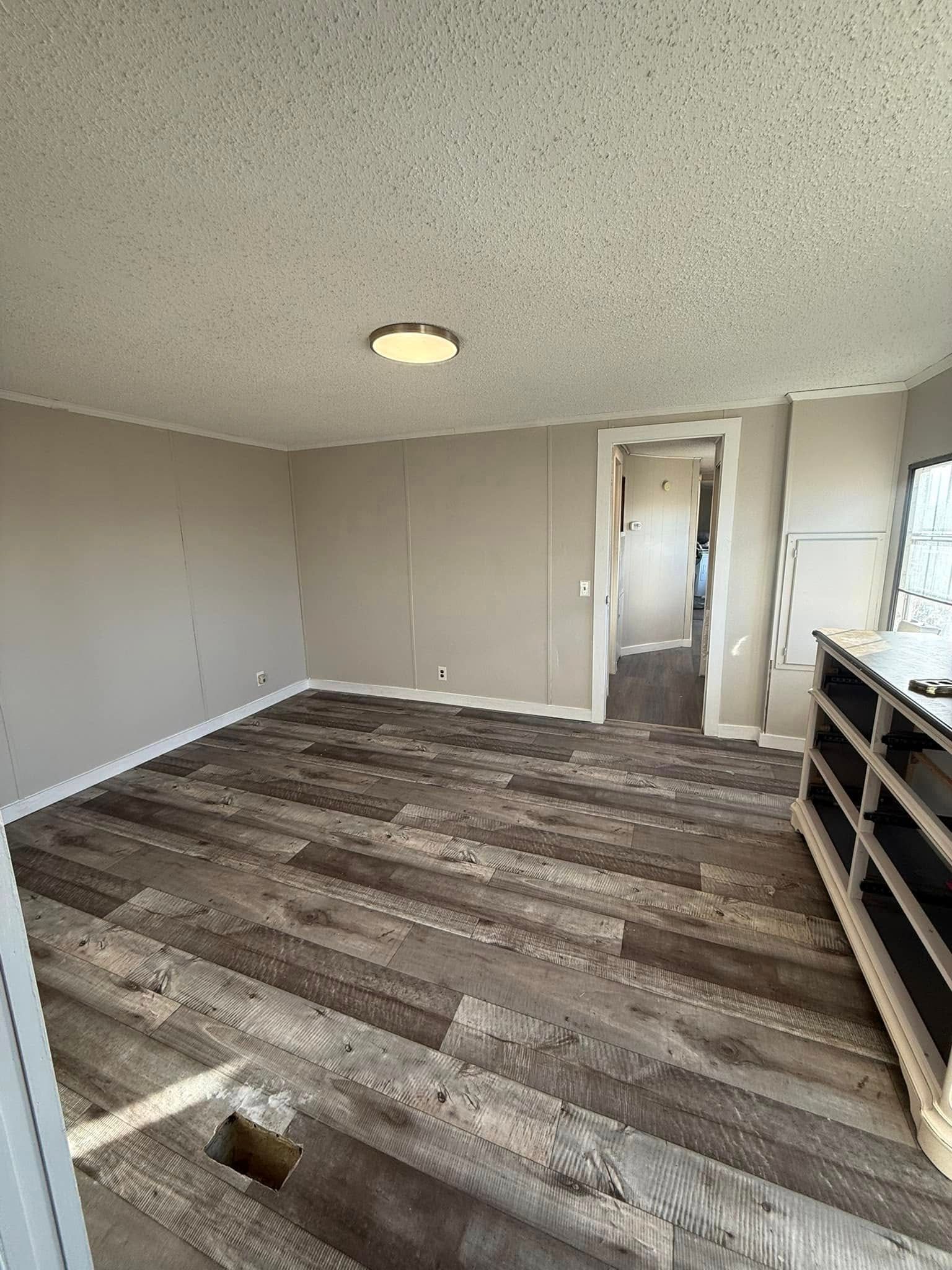An empty room with grey plank flooring, taupe walls, a textured ceiling, and a doorway leading to another area.