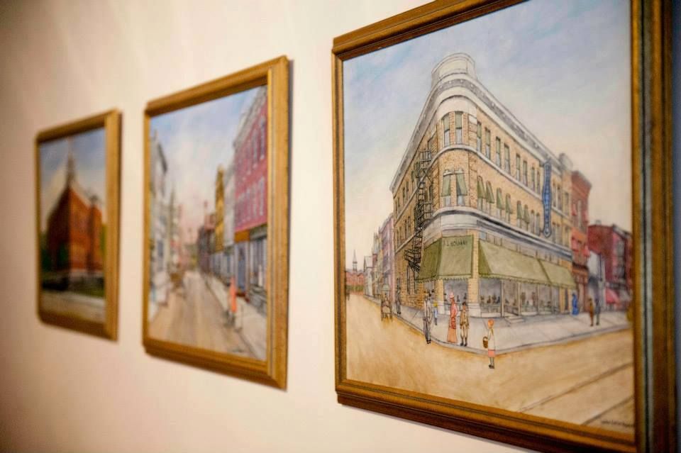 Three paintings are hanging on a wall with a building in the background.