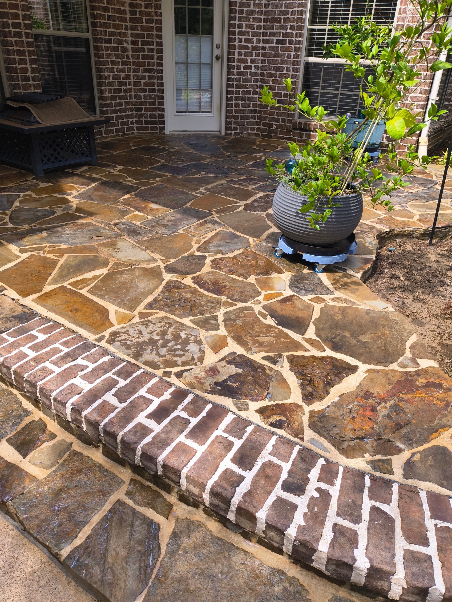Flagstone patio with brick edging, a potted plant, and a white door in a brick-walled setting.