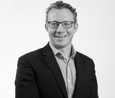 Smiling person in glasses wearing a dark blazer against a white background