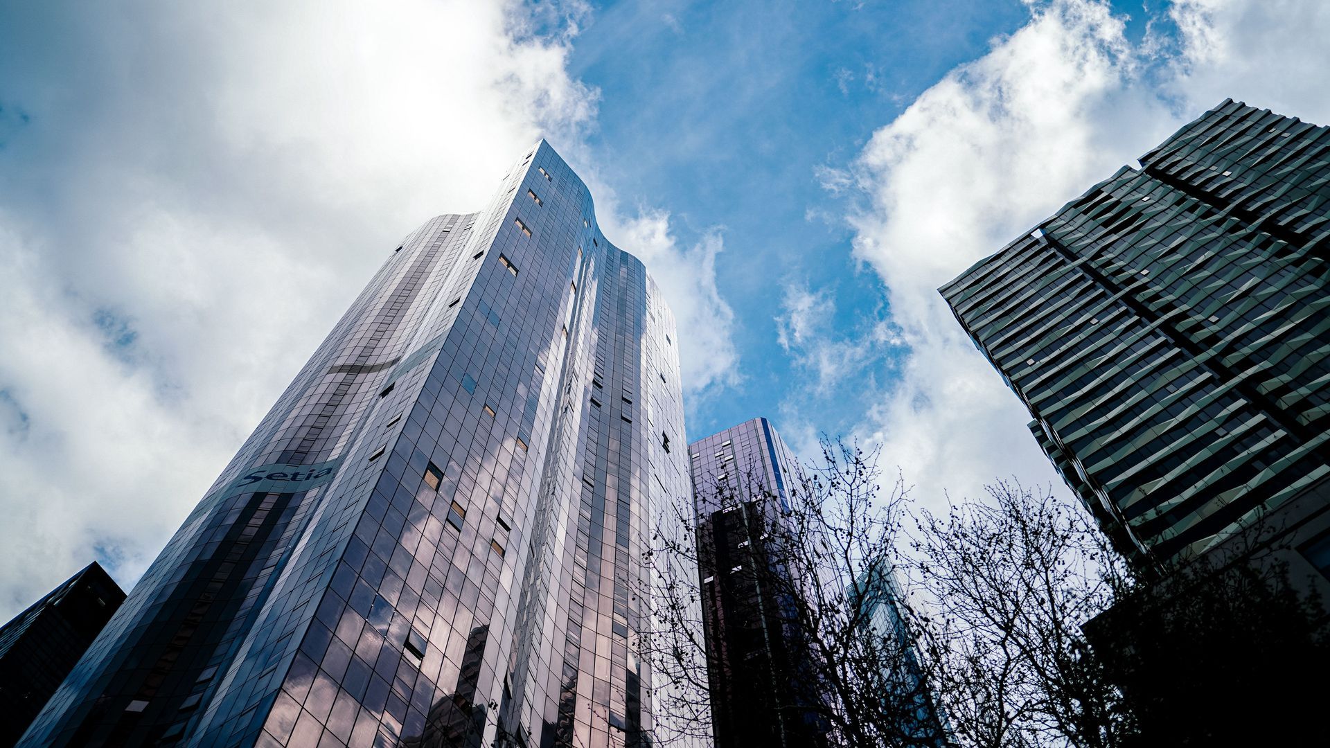 Tall glass skyscrapers viewed from below against a blue sky with clouds