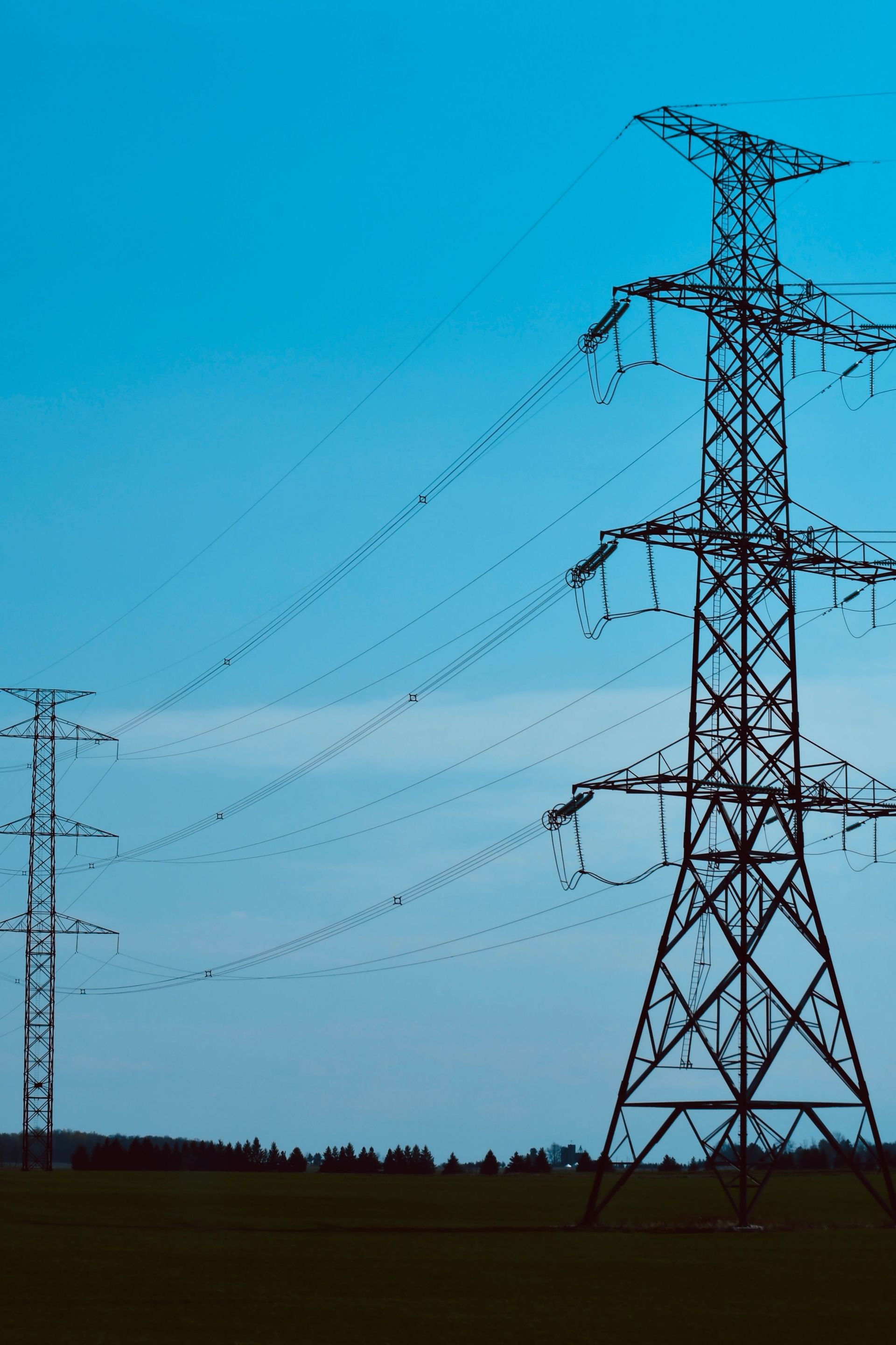 Tall power transmission tower with power lines against a blue sky over a dark field