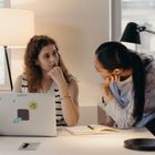 Two women talking in front of an open laptop
