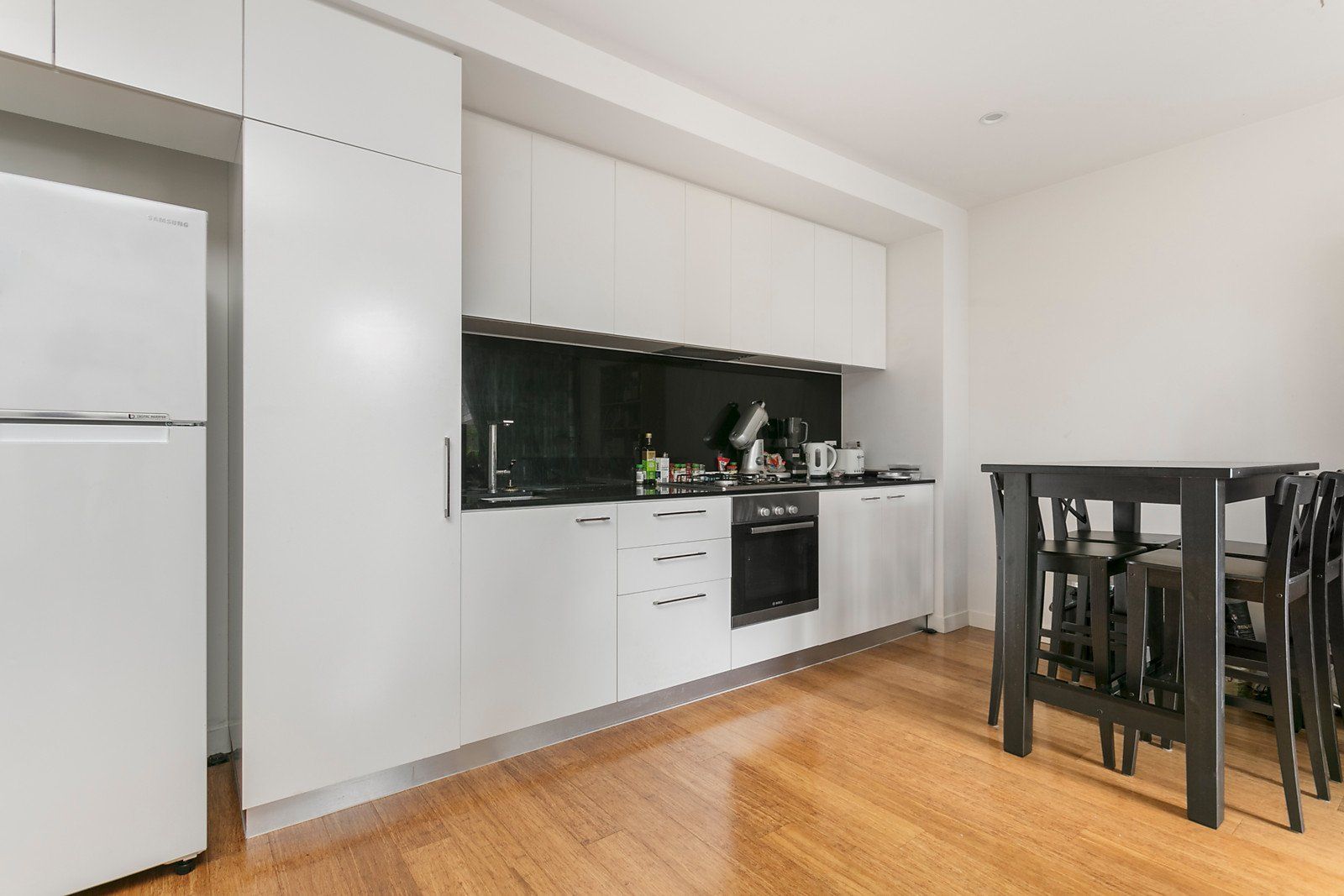 A kitchen with white cabinets , a refrigerator , a table and chairs.