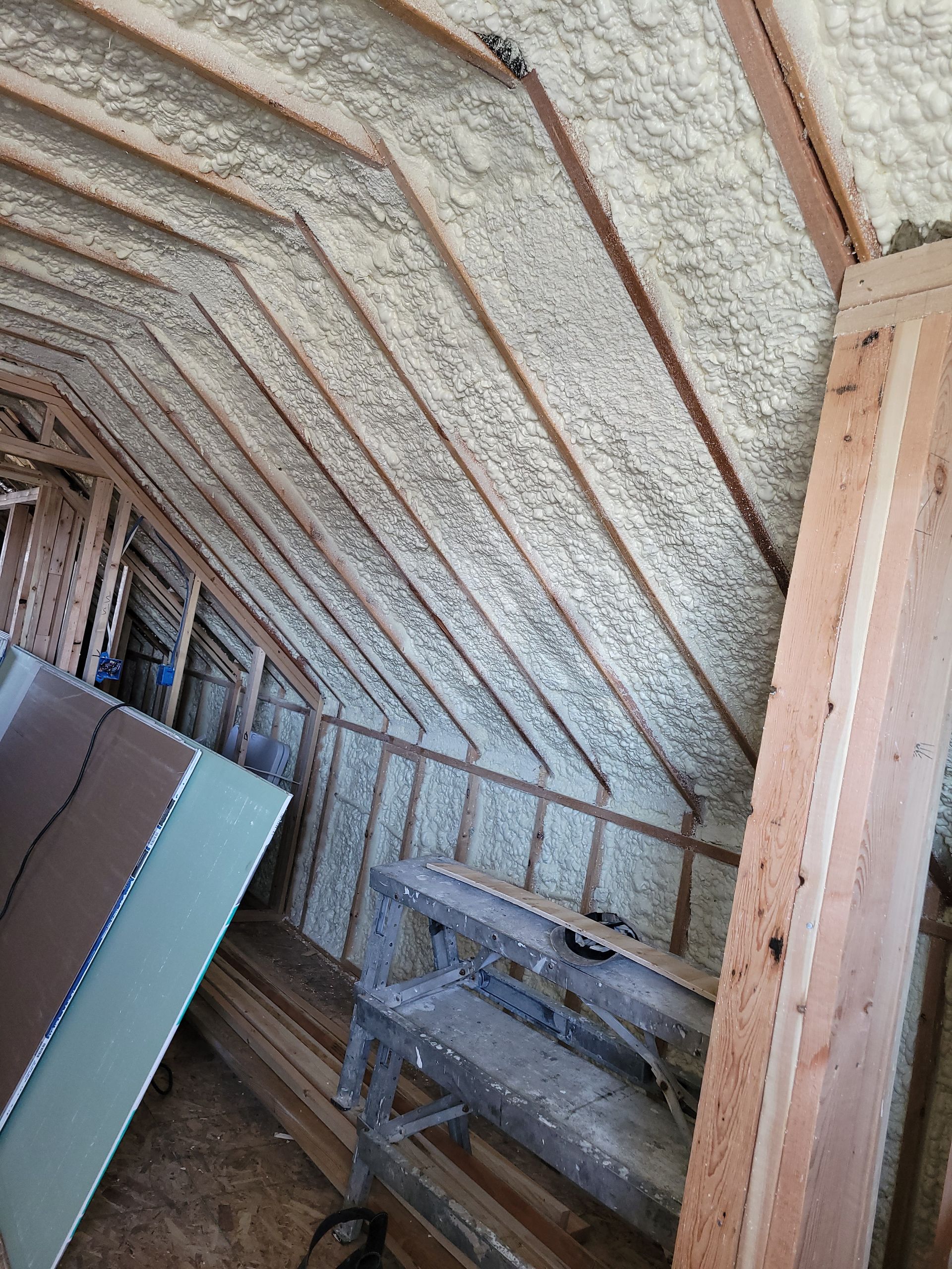 The interior of an attic under construction with sloped walls insulated by spray foam between exposed wooden studs.