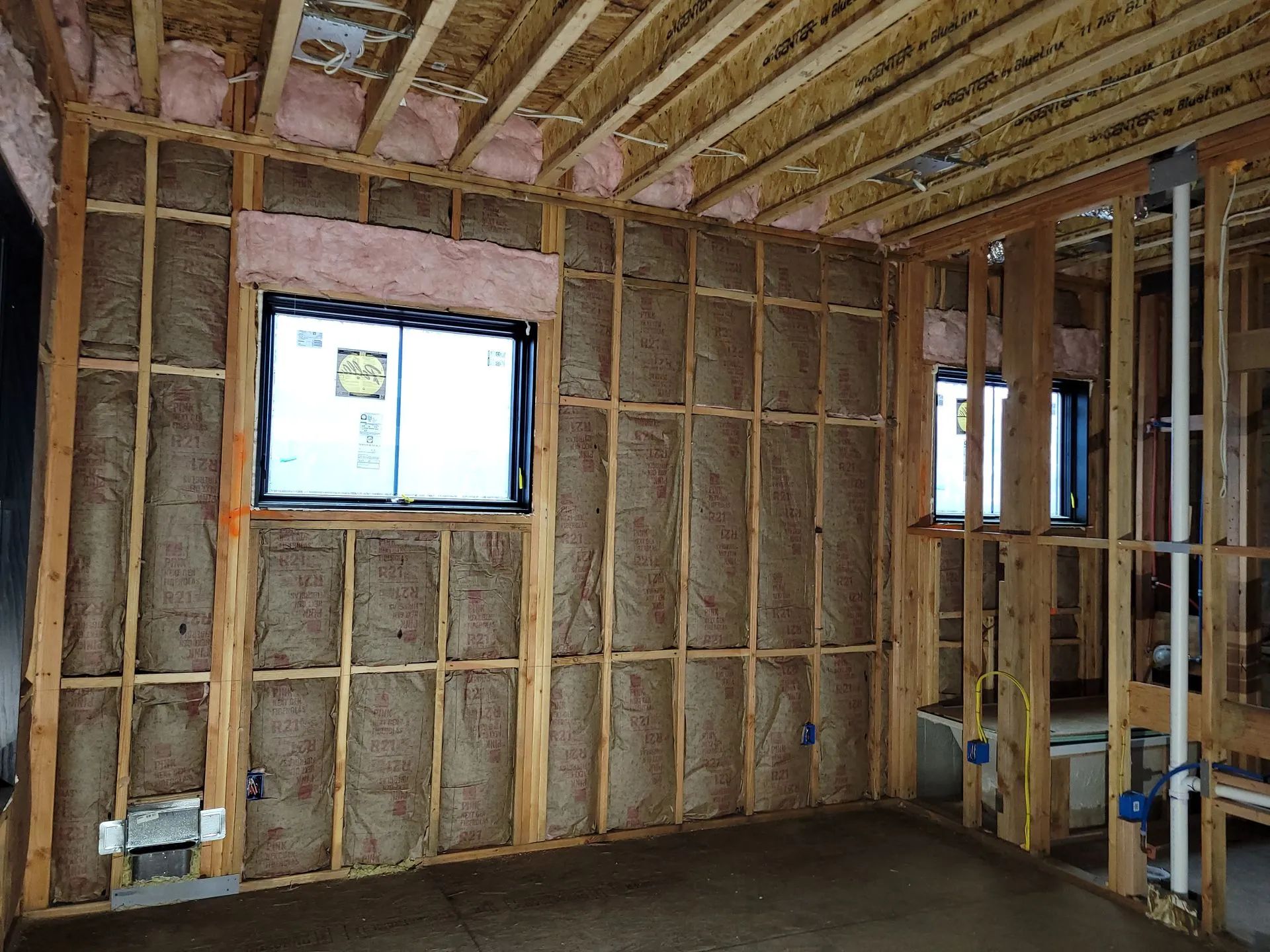 Interior wall framing in an unfinished room with exposed insulation and a small window.