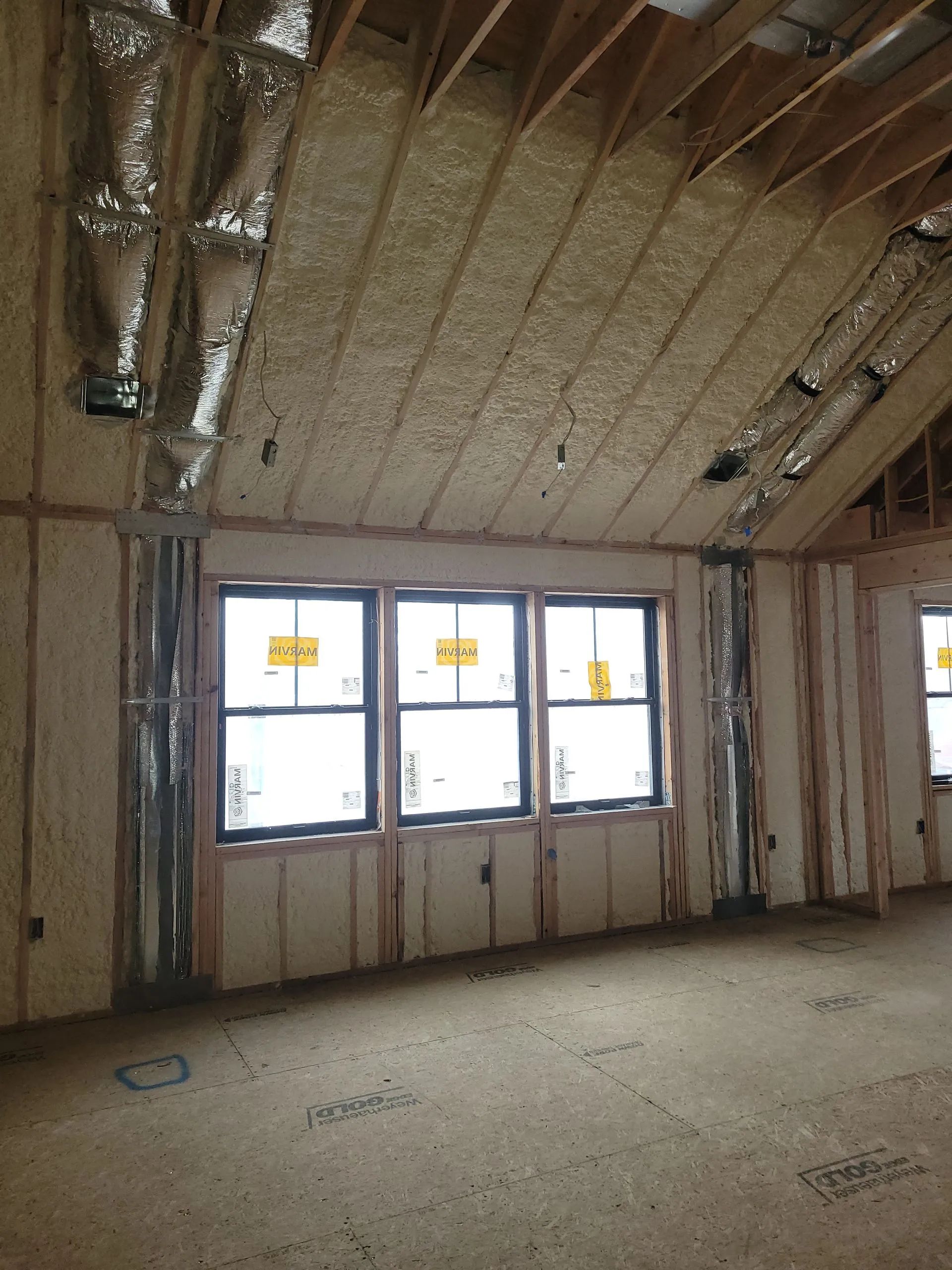 Unfinished room with exposed insulation, bare walls, and three windows letting in bright light.