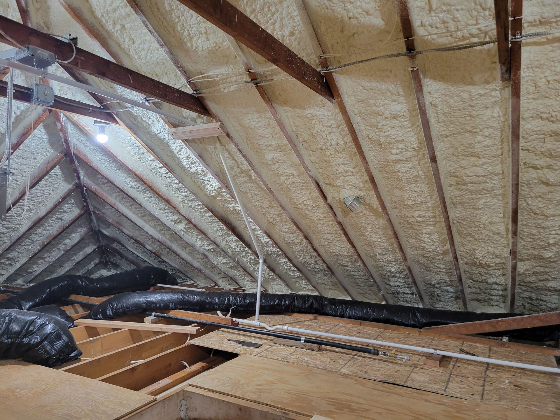 Attic with exposed insulation, wooden rafters, and partially removed flooring