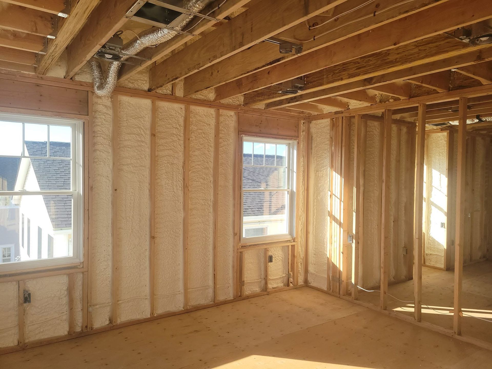 Empty unfinished room with exposed wooden framing, ceiling joists, and daylight through windows.