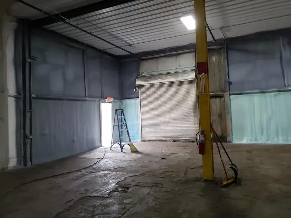 An empty warehouse with a ladder , broom , and fire extinguisher.