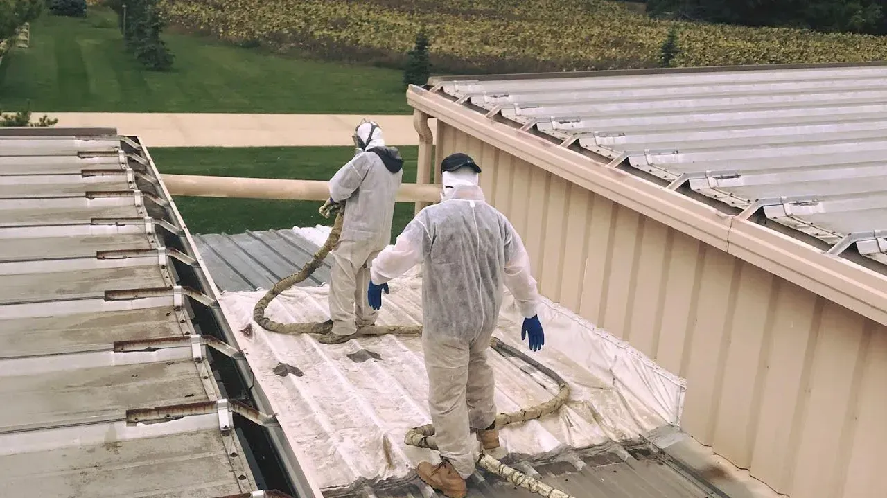 Two men are spraying foam on the roof of a building.