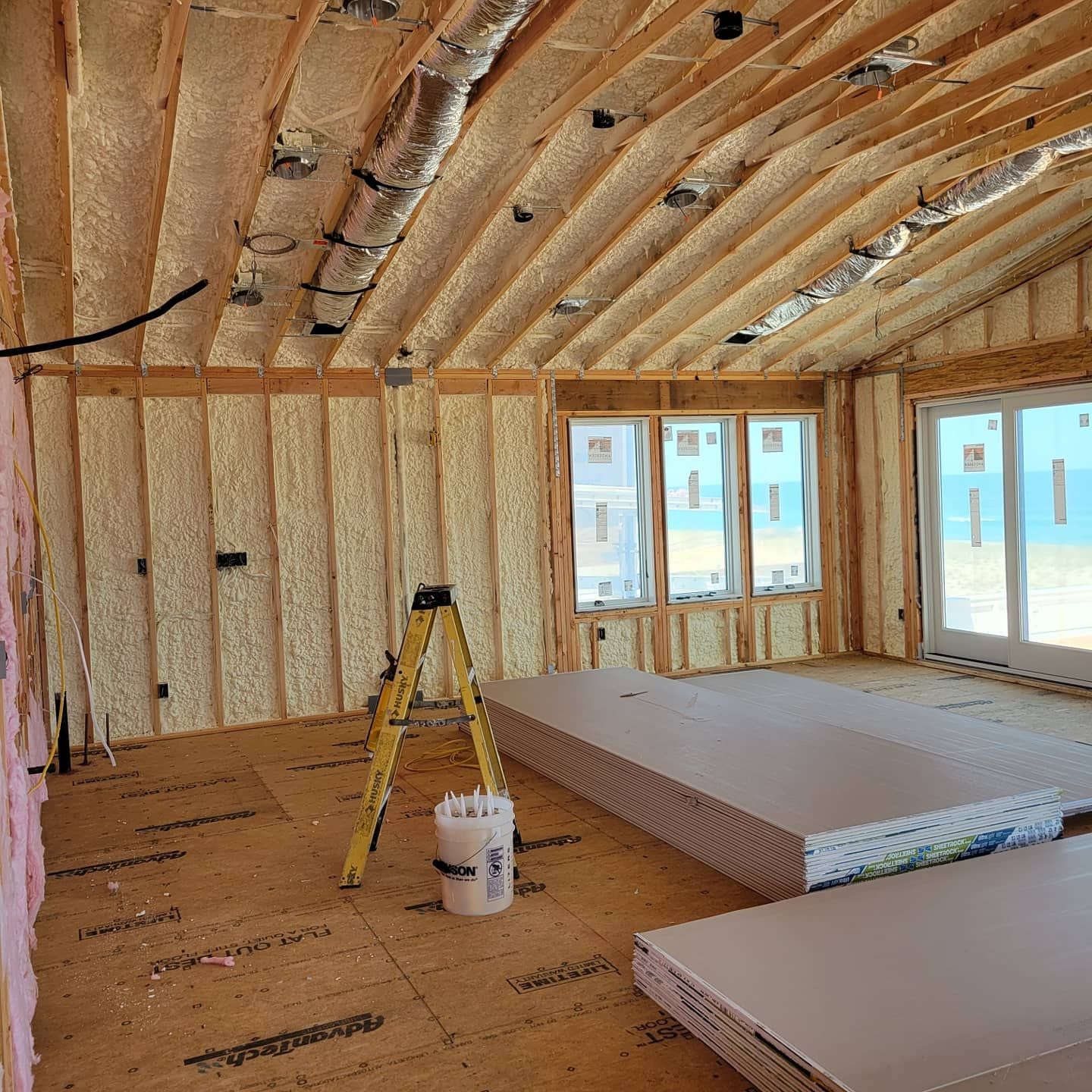 A room under construction with a ladder and a bucket on the floor.