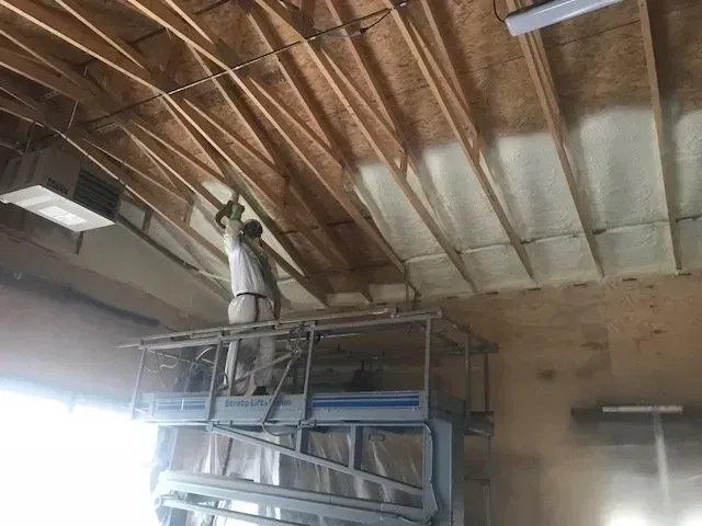 A man is spraying foam on the ceiling of a building.