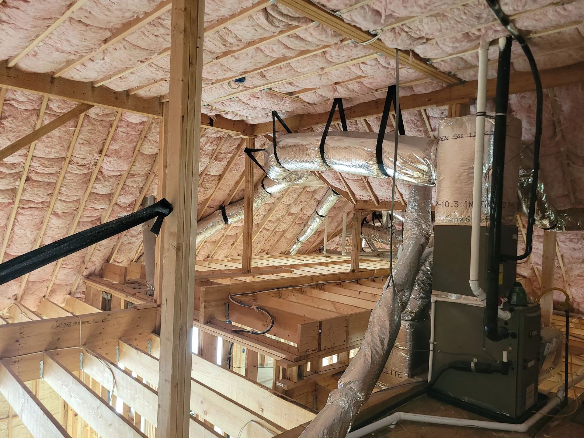 Attic with spray foam insulation, exposed wooden framing, ducts, and HVAC equipment.