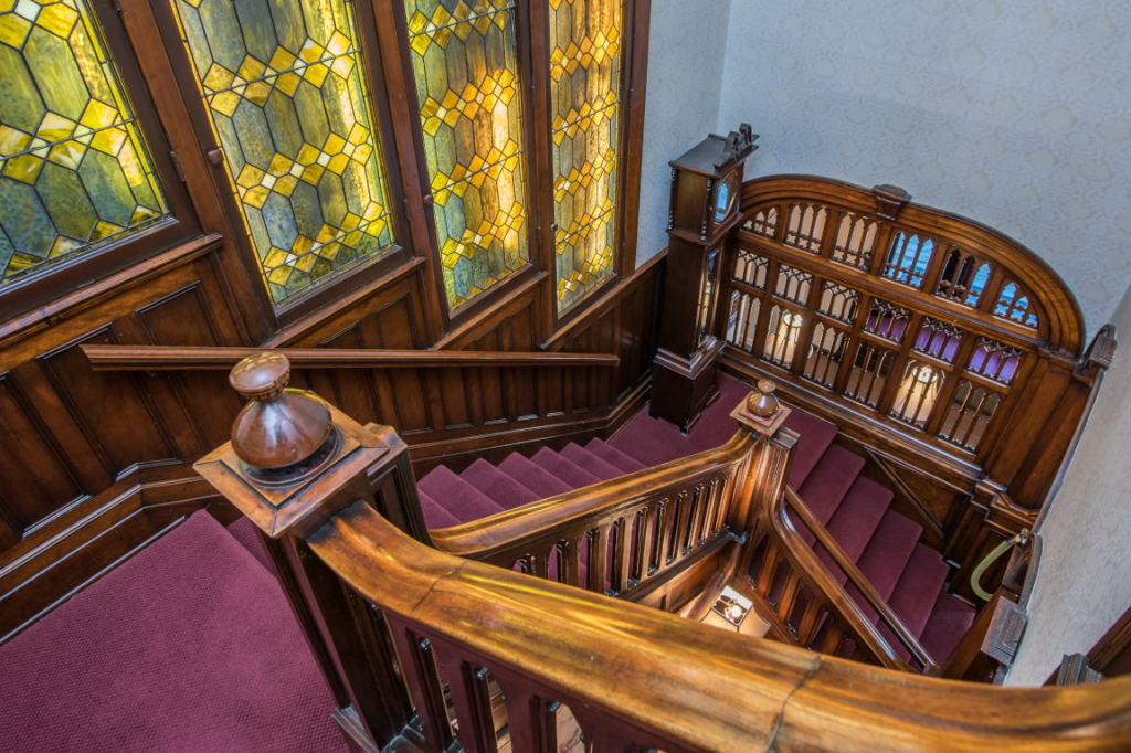 Wooden staircase with purple carpet beside stained-glass windows in a historic interior