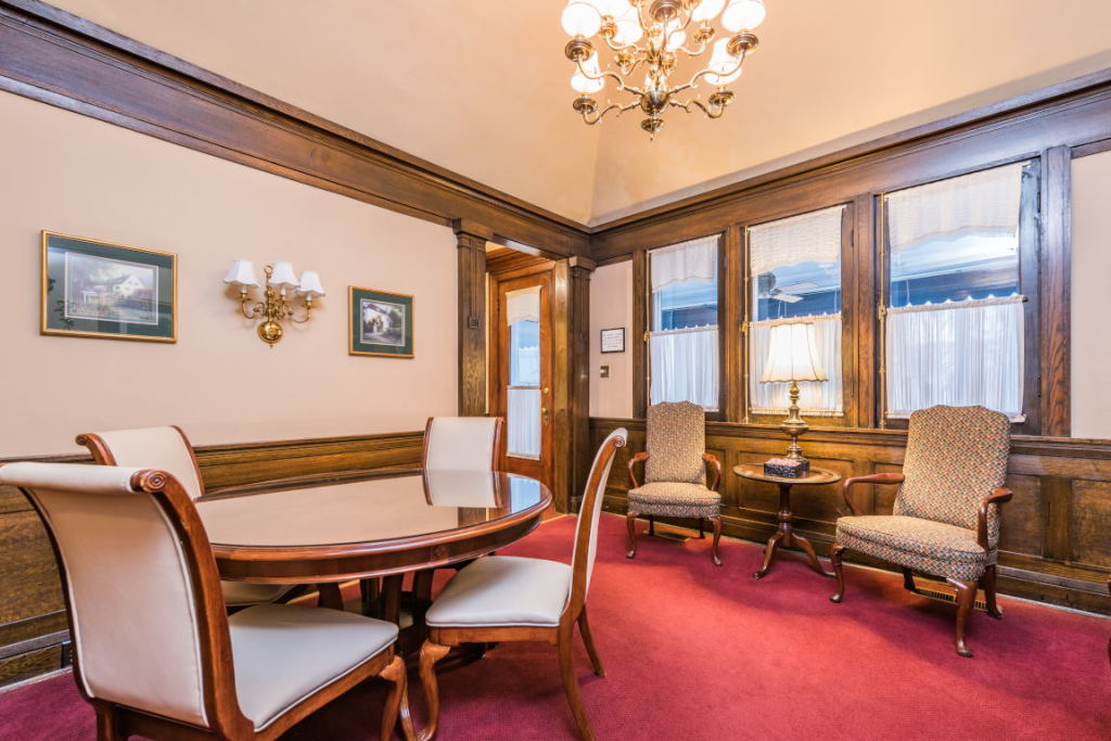 Elegant living room with red carpet, wooden table, upholstered chairs, and chandeliers by large windows