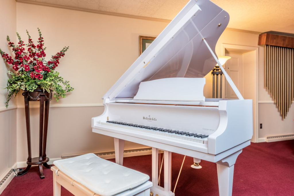 White grand piano on a red carpet in a formal room with a floral arrangement nearby