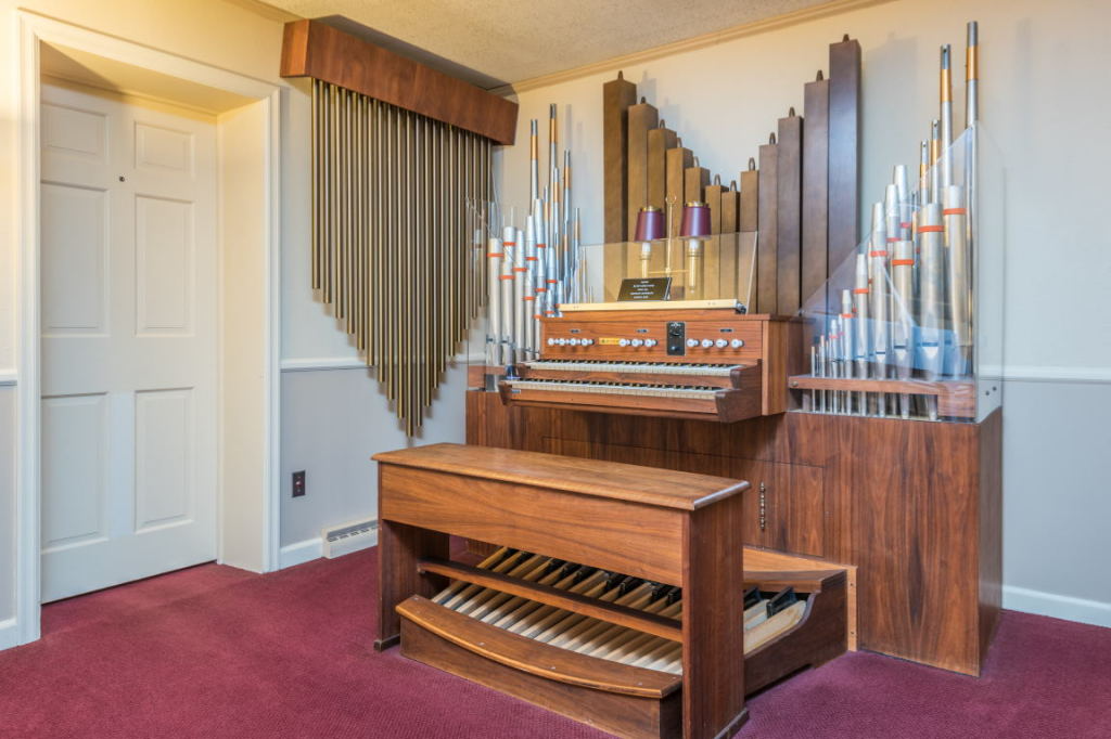 Church pipe organ with wooden console and pedals in a room with red carpet and closed white door