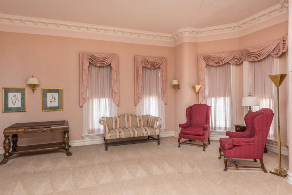 Elegant pink living room with draped windows, ornate chairs, sofa, and a wooden side table