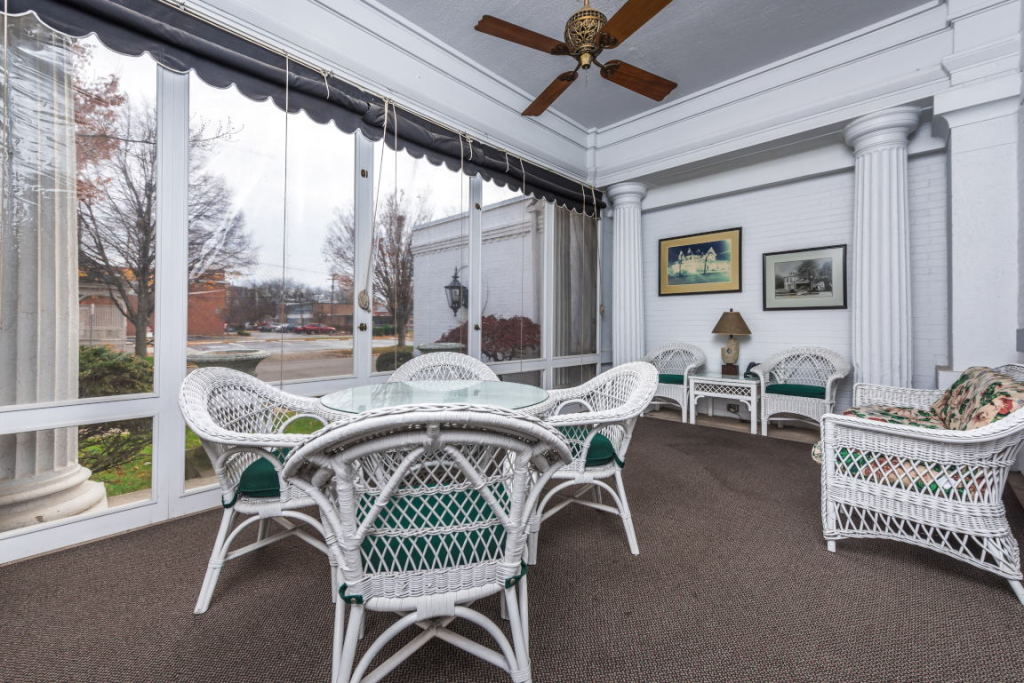 White screened porch with wicker chairs, table, ceiling fan, and large windows overlooking a winter yard