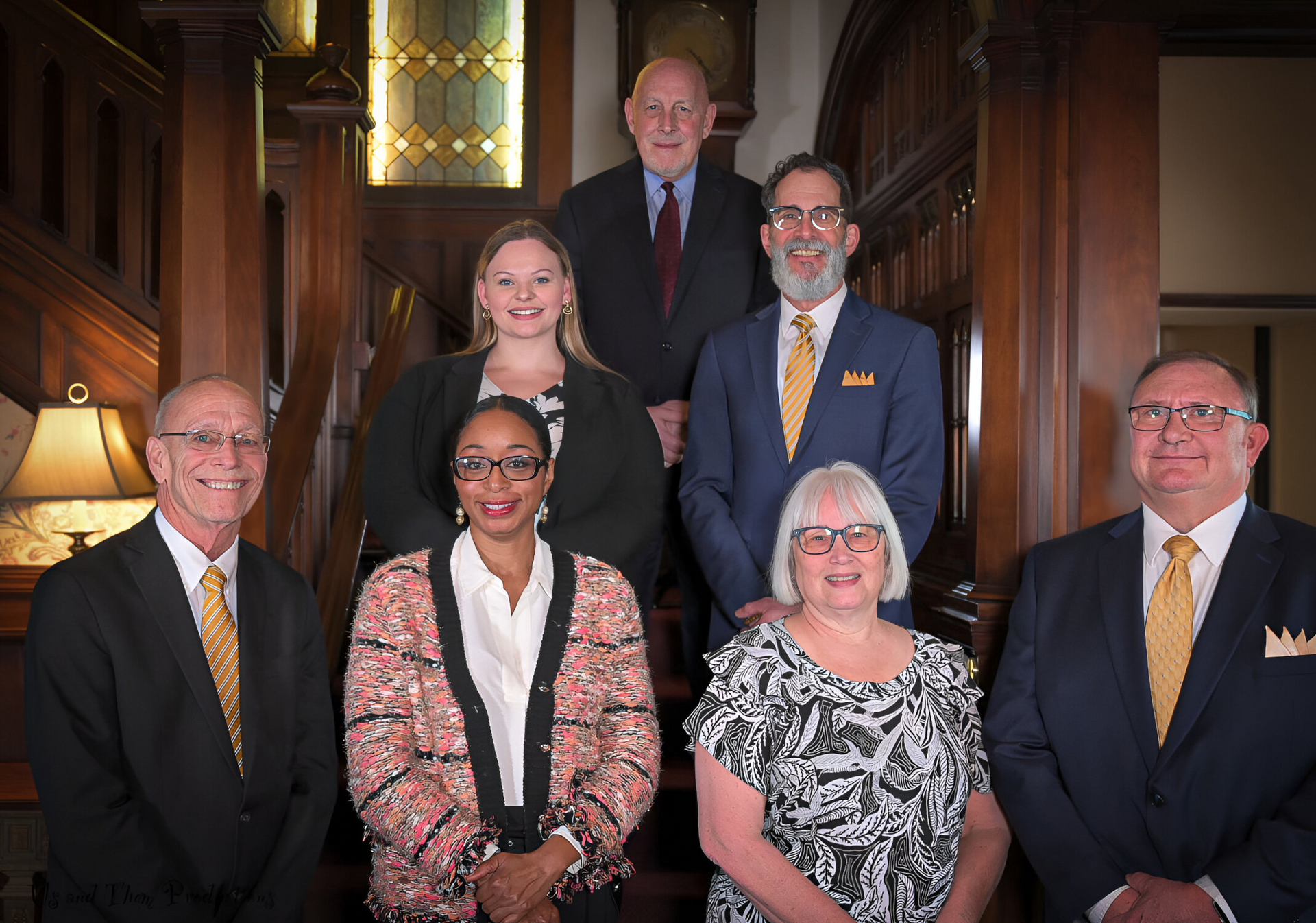 Seven people in business attire posing on a staircase in a wood-paneled building