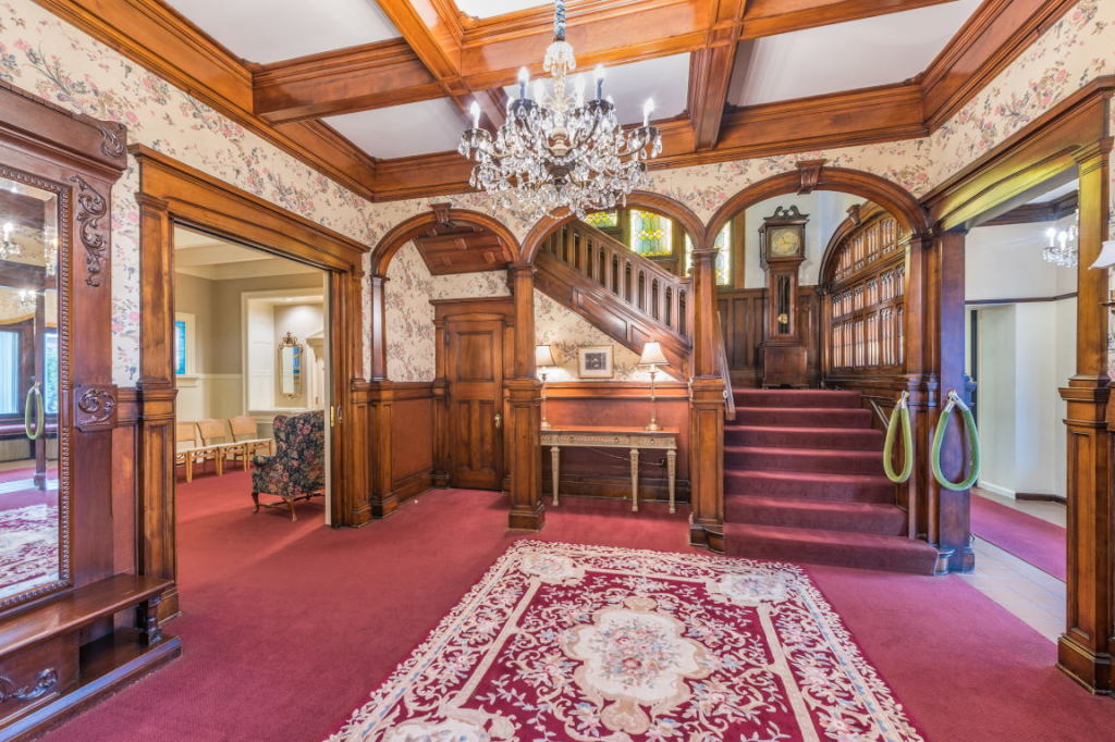 Elegant historic foyer with red carpet, carved wood paneling, chandelier, and staircase