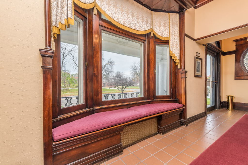 Wood-paneled hallway with a large cushioned window seat, red rug, and tiled floor in a rustic interior