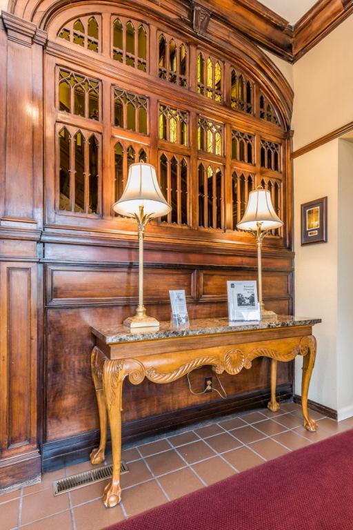 Elegant wooden hallway with carved console table, two lamps, and a framed display in a tiled interior.