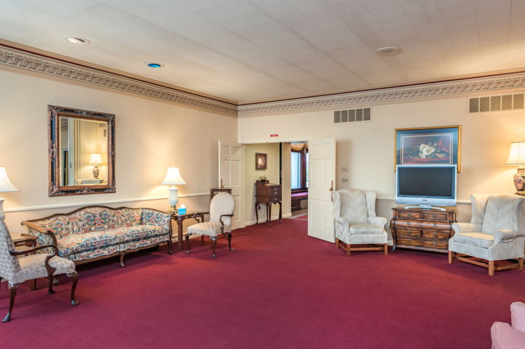 Elegant living room with maroon carpet, floral sofa, lamps, chairs, and a large mirror on the wall