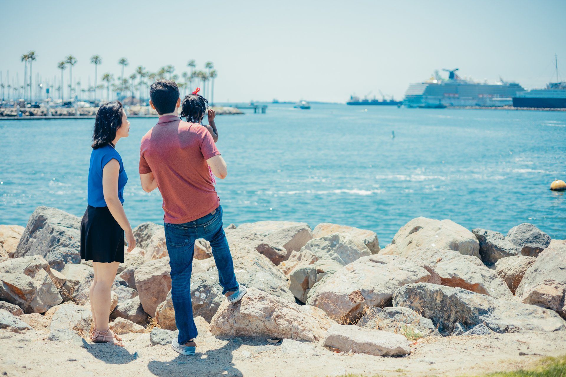 A man and a woman are standing on a rocky shoreline looking at the ocean.