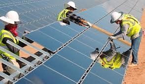 Workers installing solar panels on a rooftop, wearing hard hats and safety vests.