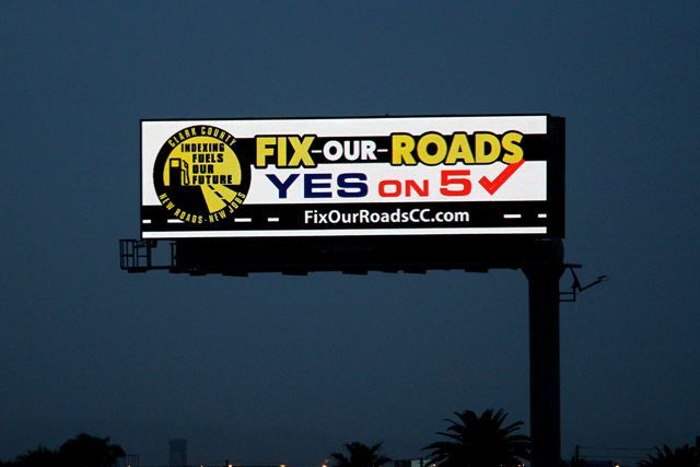 Billboard at dusk reading “FIX OUR ROADS, YES on 5” against a dark sky