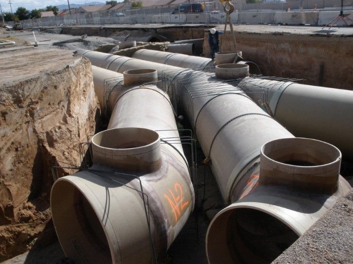 Large gray underground utility pipes in a trench at a construction site