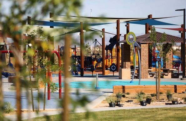 Outdoor playground with colorful climbing structures, swings, and a blue splash pad on a sunny day
