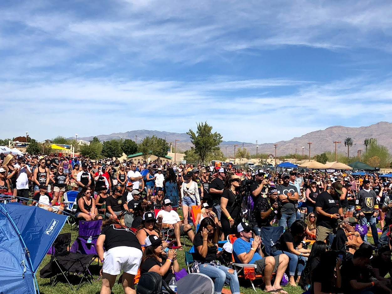 Large crowd gathered outdoors under a blue sky, with mountains in the background.