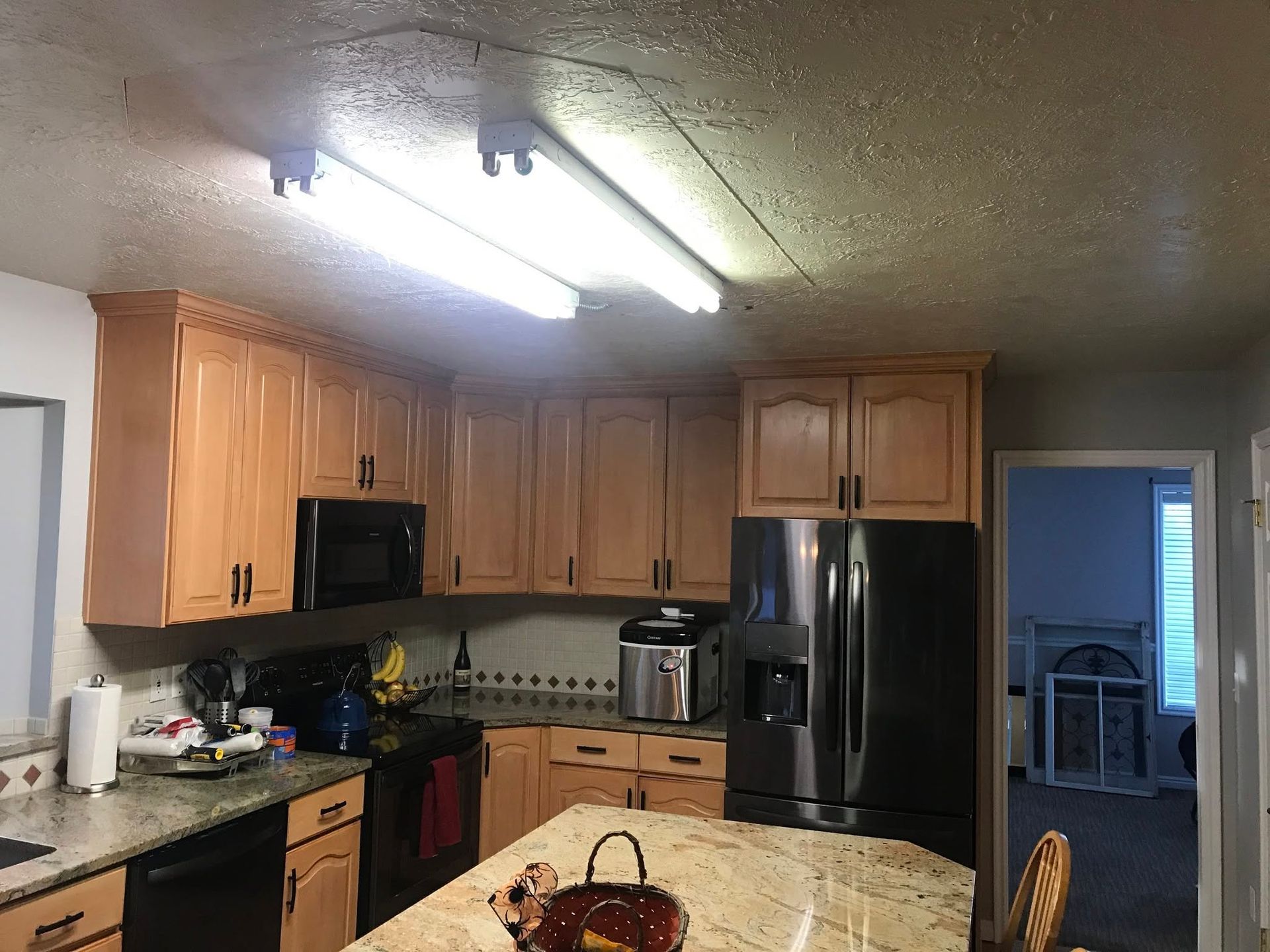 Kitchen with wooden cabinets, black appliances, granite counters, and a central island under fluorescent lights