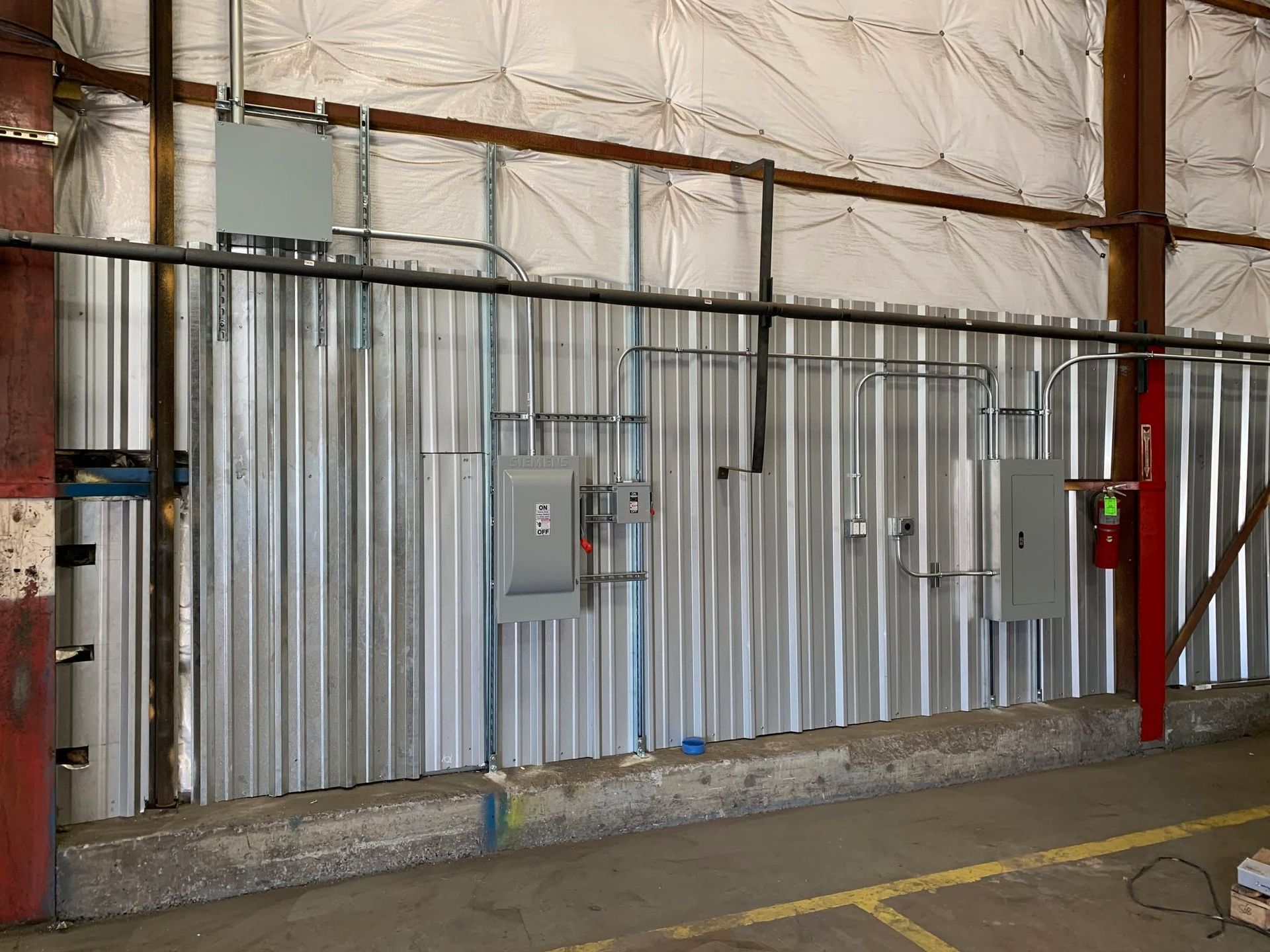 Industrial interior with corrugated metal wall, electrical panel, and red support posts